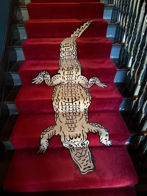 A red carpet runner with a long cream alligator design climbs a staircase with painted spindles.