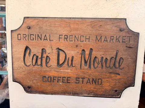 A weathered carved wooden sign reading Original French Market Cafe Du Monde Coffee Stand.