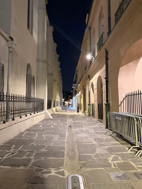 An empty flagstone alley lit at night between a cathedral wall and arched historic buildings.
