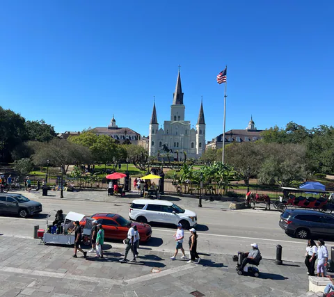 Elevated view of St. Louis Cathedral behind Jackson Square, with a flag, mule carriages and red and yellow umbrellas.