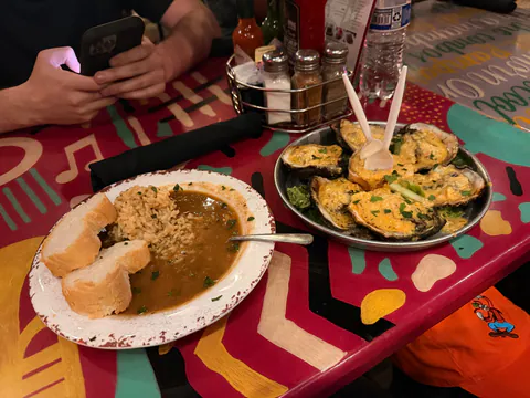 Chargrilled oysters and a bowl of gumbo with rice and French bread on a colorful painted table.