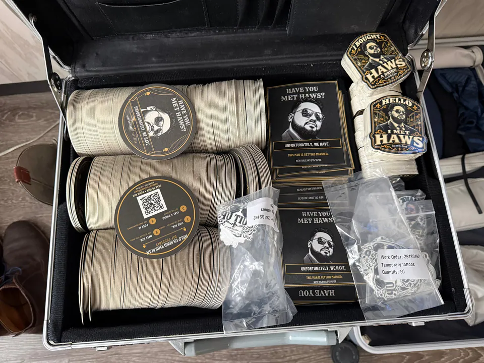 An open silver briefcase packed with Have You Met Haws coasters, table cards, stickers and bagged temporary tattoos.